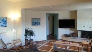 A living room with a sofa, a coffee table, a TV, and a fireplace. There is a door leading to another room. - Dream apartment in a top location directly on the beach, with beautiful sea views (Λυγαριά)