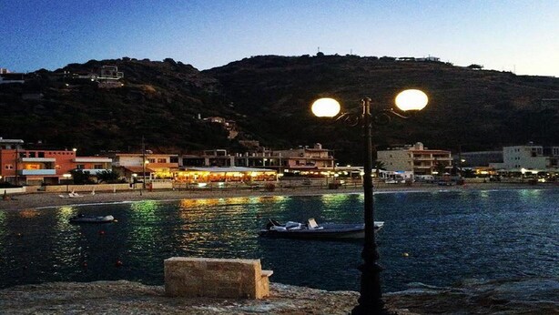 A coastal town at dusk with a stone bench, a lamp post, and boats on the water. - Dream apartment in a top location directly on the beach, with beautiful sea views (Λυγαριά)
