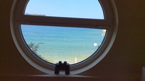 A round window with a clear view of the ocean and a small toy figure on the sill. - Dream apartment in a top location directly on the beach, with beautiful sea views (Λυγαριά)
