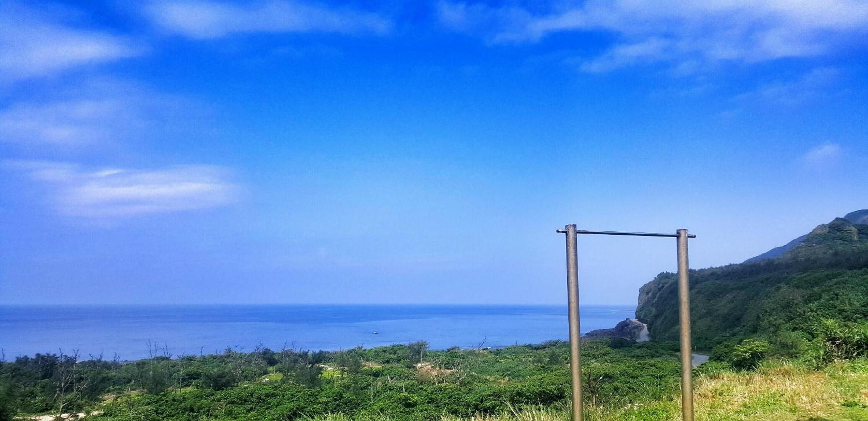 A coastal landscape with a metal structure, lush greenery, and a clear view of the ocean.
