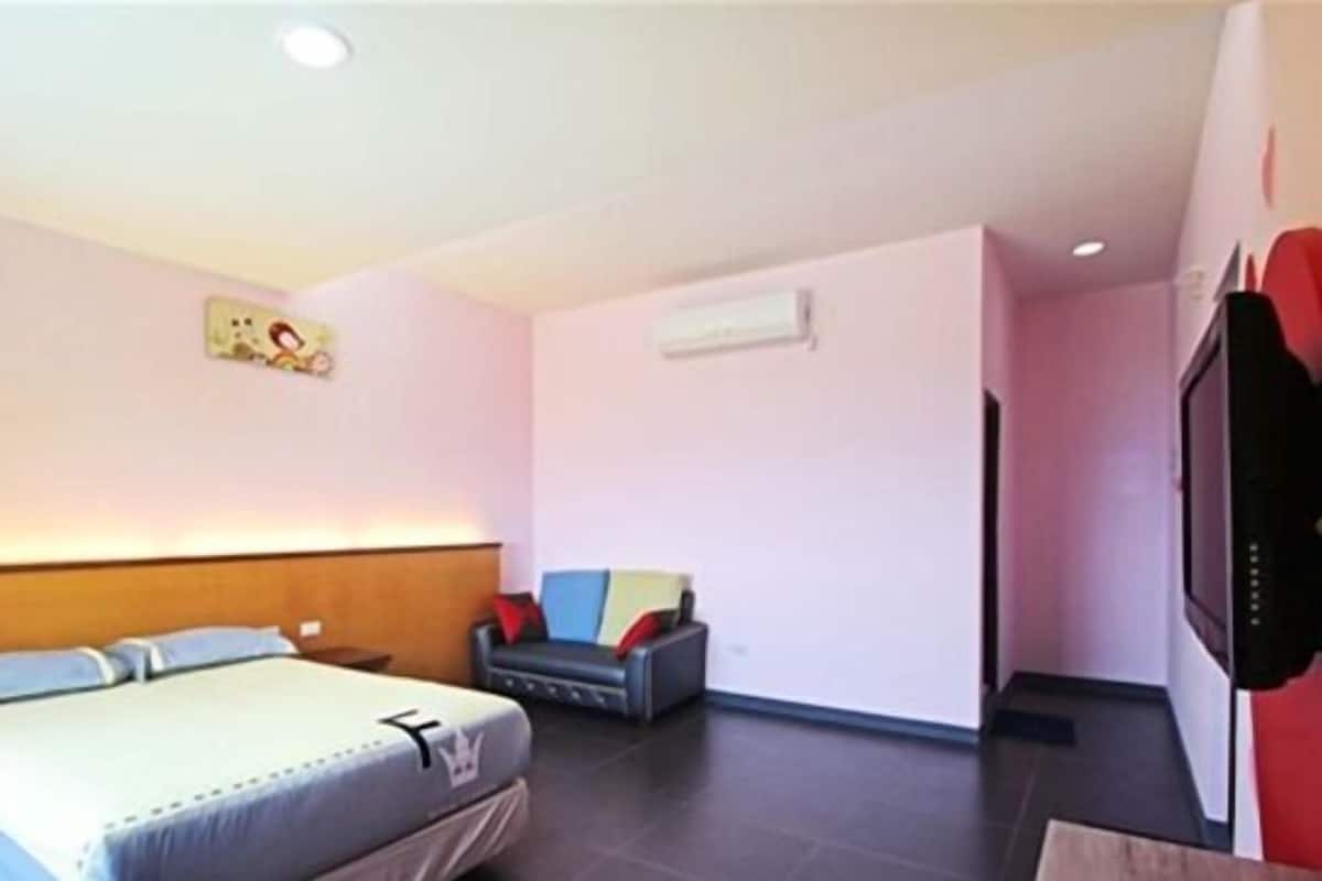 Una habitación de hotel con una cama, un pequeño sofá, un televisor y un aire acondicionado instalado en la pared.
