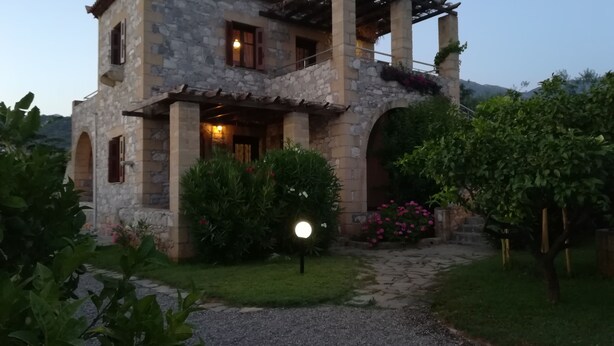 Una casa de piedra con una p érgola, una escalera de piedra y un jardín con flores y arbustos.