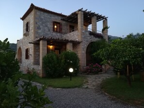 Ein Haus aus Stein mit einer Pergola, einer Steintreppe und einem Garten mit Blumen und Sträuchern.