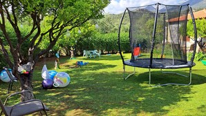 Un trampolín en un patio trasero con césped, árboles y una casa al fondo.