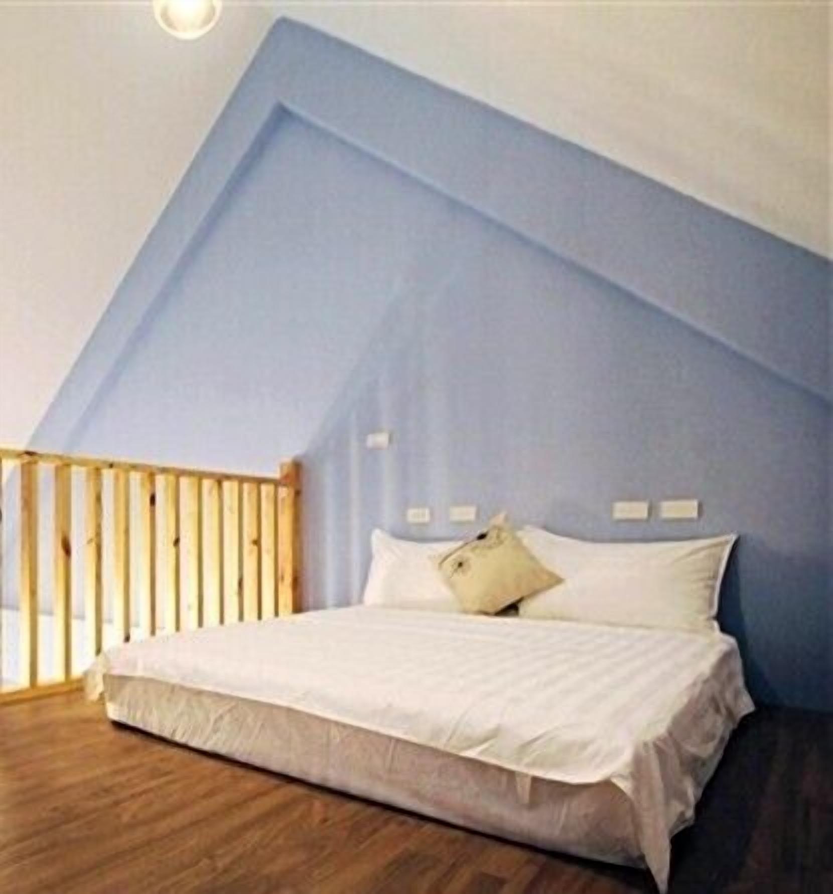 A bedroom with a sloped ceiling, a wooden bed frame, and a white mattress.