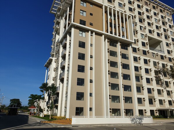 Un immeuble résidentiel à plusieurs étages, doté de balcons, d’une entrée sécurisée et surplombant un ciel dégagé.