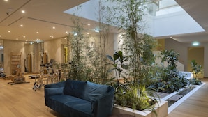 A spacious indoor area with a high ceiling, a blue sofa, and various exercise equipment. - COCO-MAT Athens BC (Athens)
