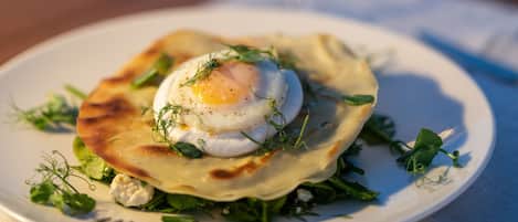 Une assiette de nourriture comprenant un œuf poché, des légumes verts et du fromage, le tout présenté sur une assiette blanche, avec un verre de vin blanc en arrière-plan.