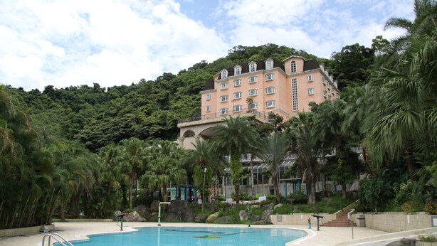 A swimming pool with a curved edge, surrounded by palm trees and a large building in the background. - Life Leisure Resort (Guanxi)