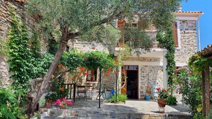 A stone courtyard with a rustic building, a wooden table, and potted plants.