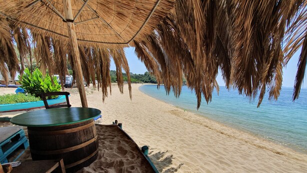 A beachside seating area with a thatched umbrella, wooden table, and chairs.