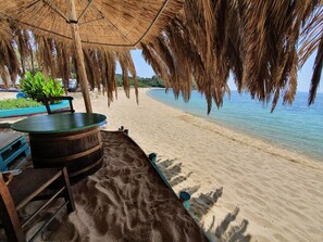 A beachside seating area with a thatched umbrella, wooden table, and chairs. - Traditional stone house with enclosed, idyllic courtyard, near the sea (Νικήτη)