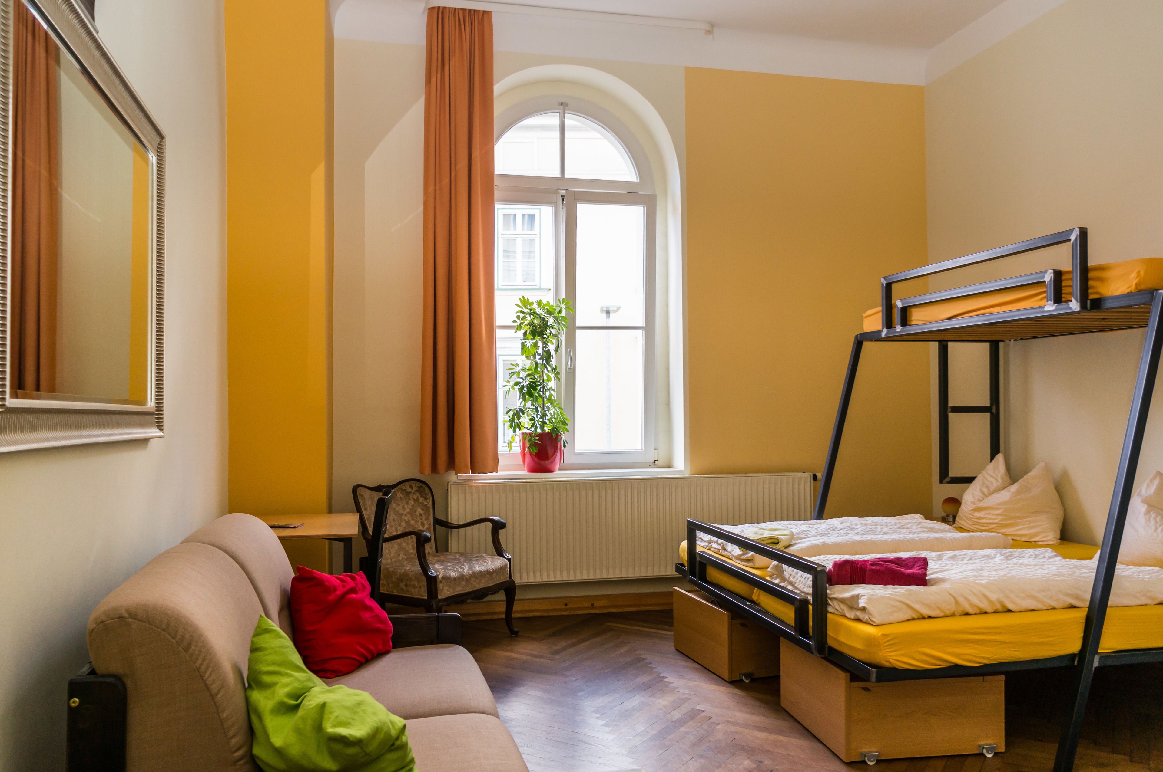 Una habitación con una cama litera, un sofá, una silla, un radiador y una ventana con cortinas.