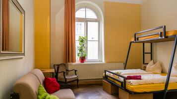 Una habitación con una cama litera, un sofá, una silla, un radiador y una ventana con cortinas.