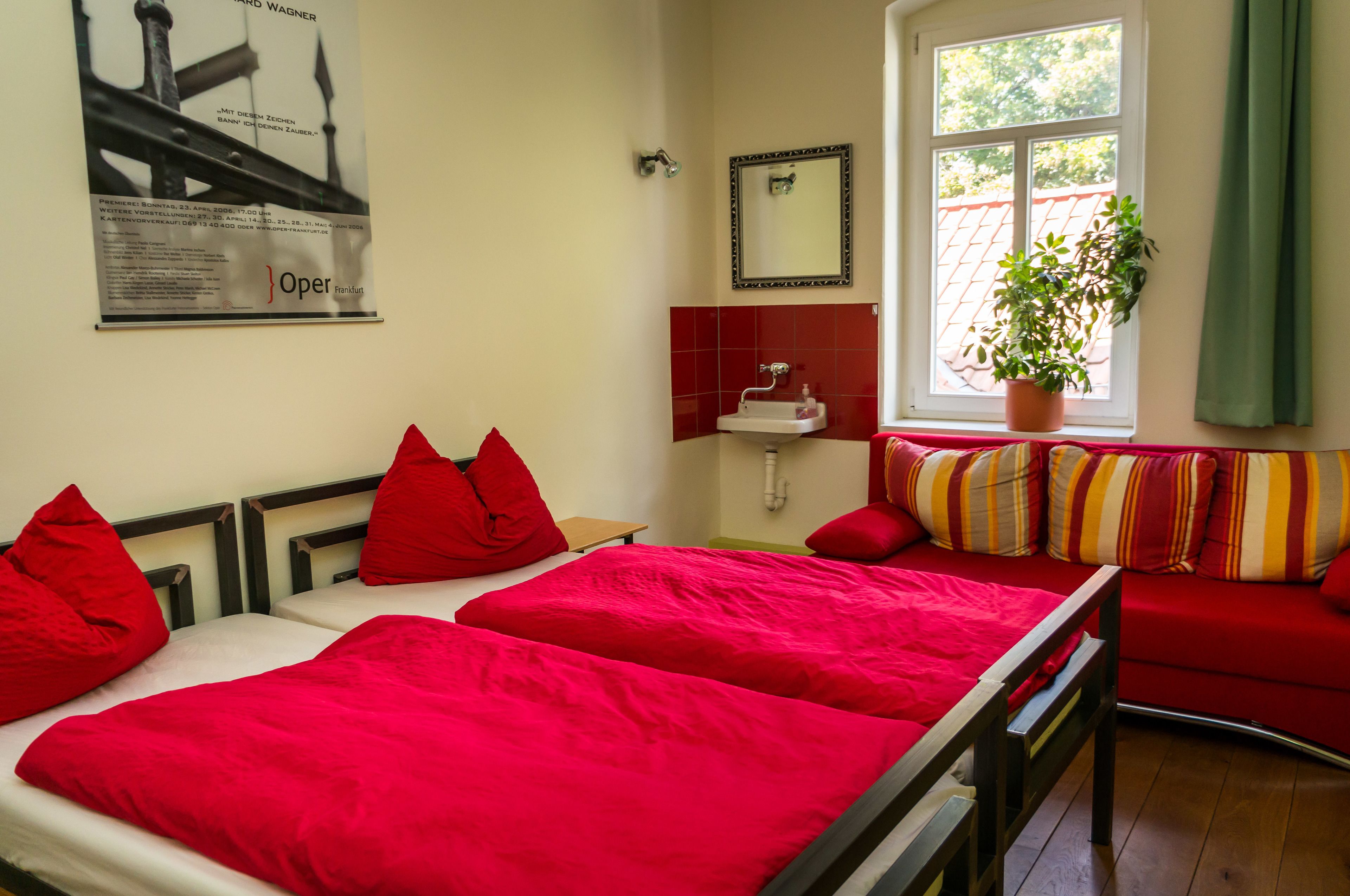 Habitación de hotel con dos camas, un sofá rojo, una ventana con vistas, un lavamanos y un espejo.