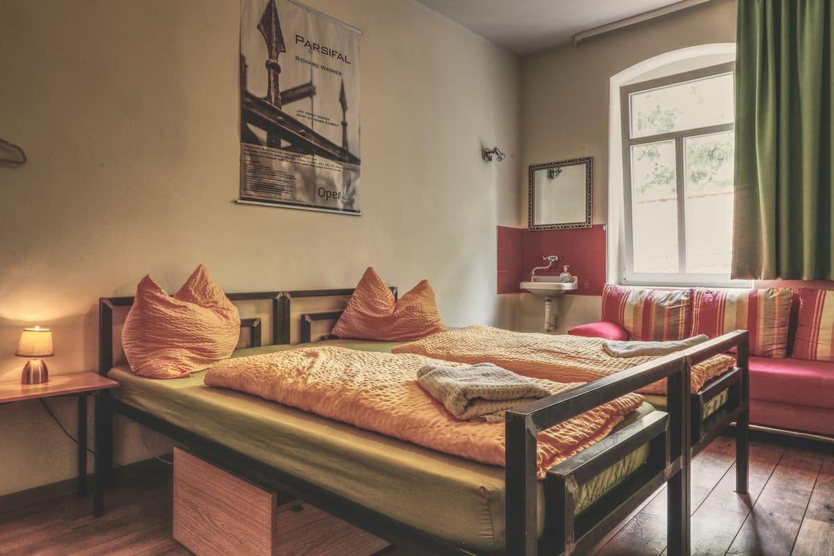 A bedroom with a wooden bed, a nightstand with a lamp, a window with curtains, and a poster on the wall.