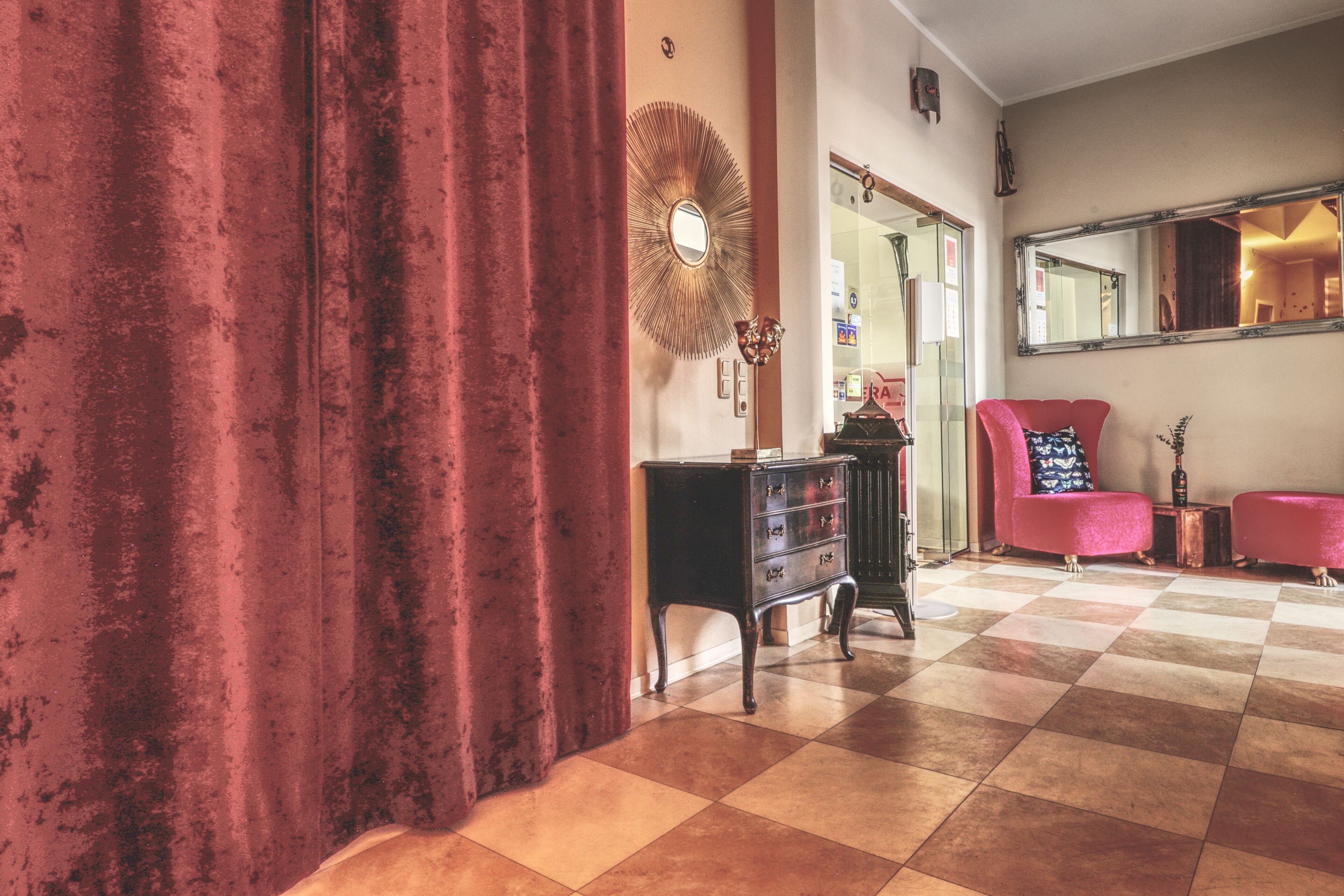 Una habitación con suelo a cuadros, una cortina roja, un espejo, un aparador y dos sillas.