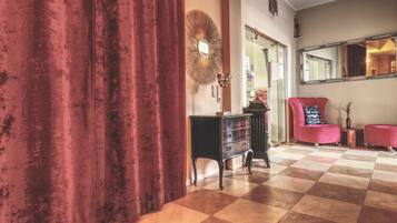 Una habitación con suelo a cuadros, una cortina roja, un espejo, un aparador y dos sillas.