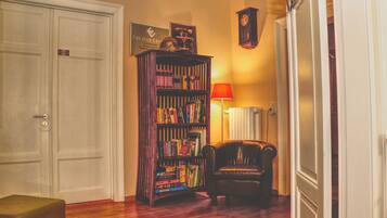 Una habitación con una estantería, un sillón de cuero, una lámpara y un reloj en la pared.