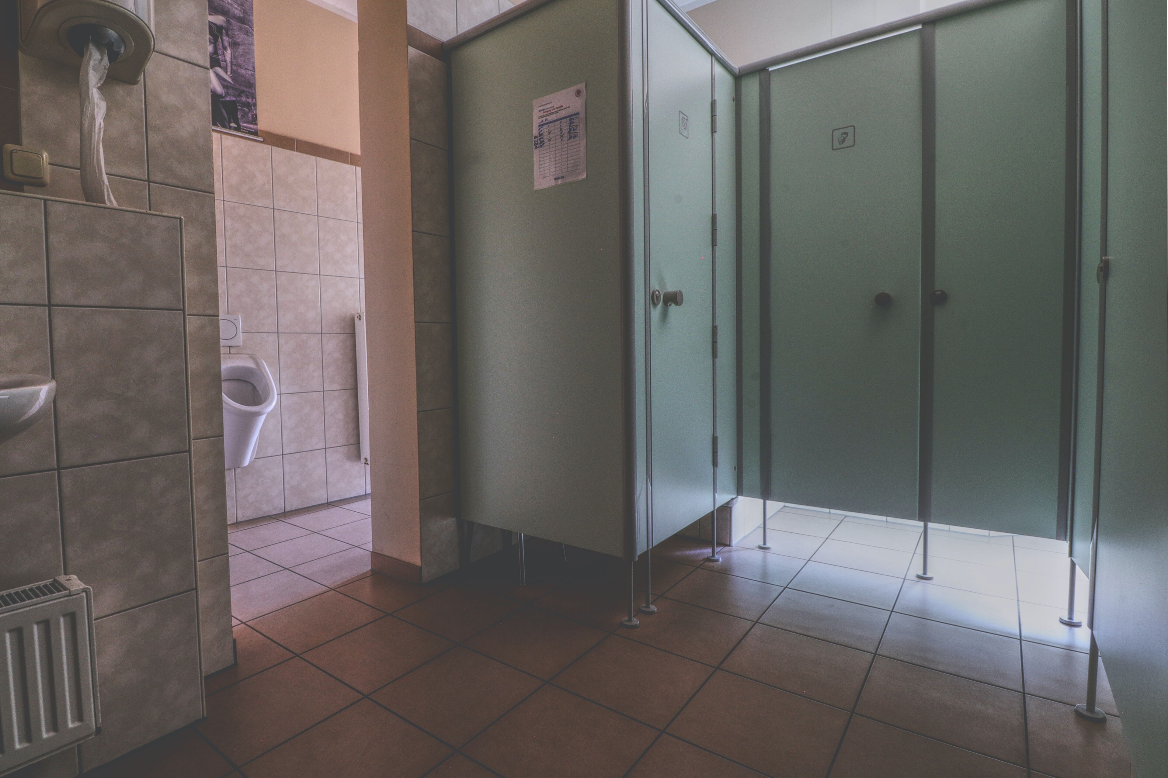 Des toilettes comprenant un urinoir, un distributeur de papier et une cabine verte assurant l’intimité.