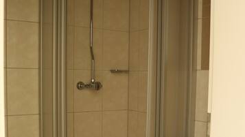 A shower enclosure with a glass door, a showerhead, and a sink to the right.