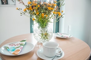A table with a white cup and saucer, a folded napkin, and a glass vase with yellow flowers. - bikehikesleep (Sasbachwalden)