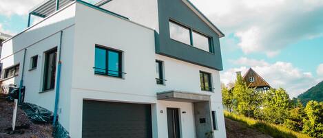 A modern two-story house with a garage, large windows, and a sloped roof.