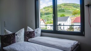 A bedroom with two beds, a large window with a view of a green landscape and buildings. - bikehikesleep (Sasbachwalden)