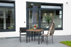 A hotel entrance with a glass door, a wooden table, two chairs, and a potted plant.