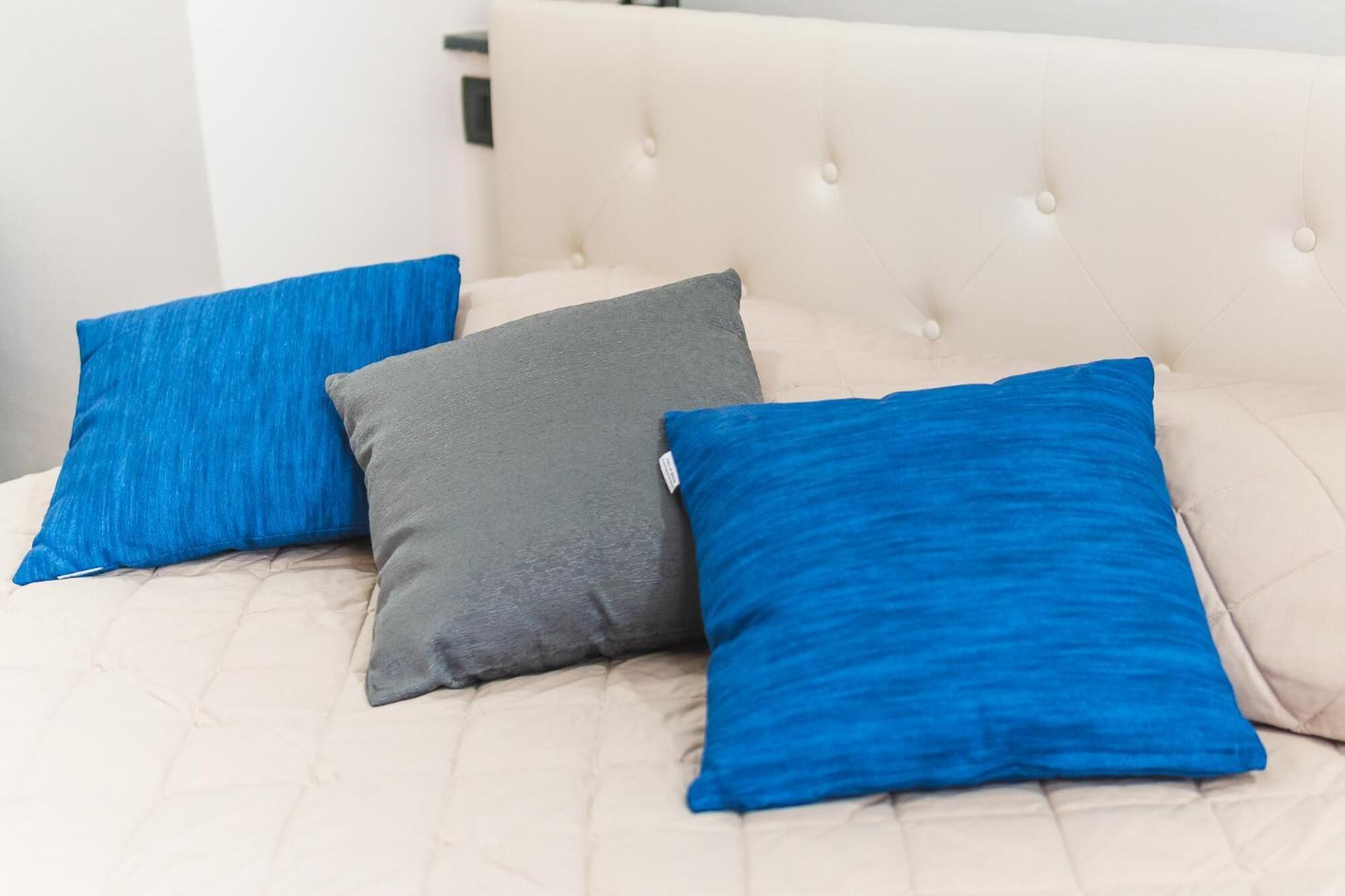 A bed with a tufted headboard and three pillows in different colors.