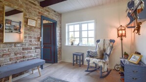 A cozy room with a brick wall, a wooden bench, a rocking chair, a small table, and a window with natural light. - Awesome home in Haderslev with WiFi (Haderslev)