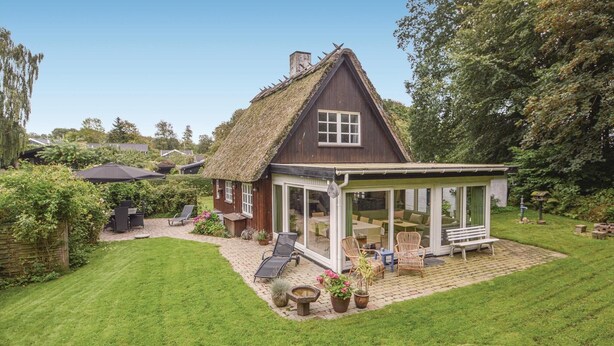 A thatched-roof house with a glass conservatory, surrounded by a well-maintained lawn and garden furniture. - Awesome home in Haderslev with WiFi (Haderslev)
