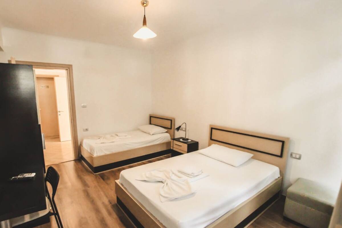 Een hotelkamer met twee eenpersoonsbedden, een bureau, een stoel, een klein tafeltje en een prullenbak.