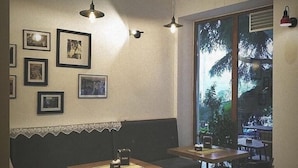 A cozy room with a wooden floor, a sofa, a table, and chairs. There are framed pictures on the wall and a window with a view of trees. - Hotel RELAX Pazari i Vjeter (Gjirokastër)