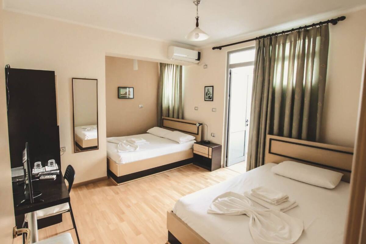 Hotelkamer met twee bedden, een bureau met stoel, een airconditioning en een raam met gordijnen.