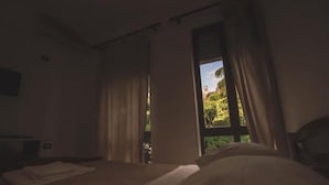 A dimly lit hotel room with a bed, curtains, and a window offering a view of greenery outside. - Hotel RELAX Pazari i Vjeter (Gjirokastër)