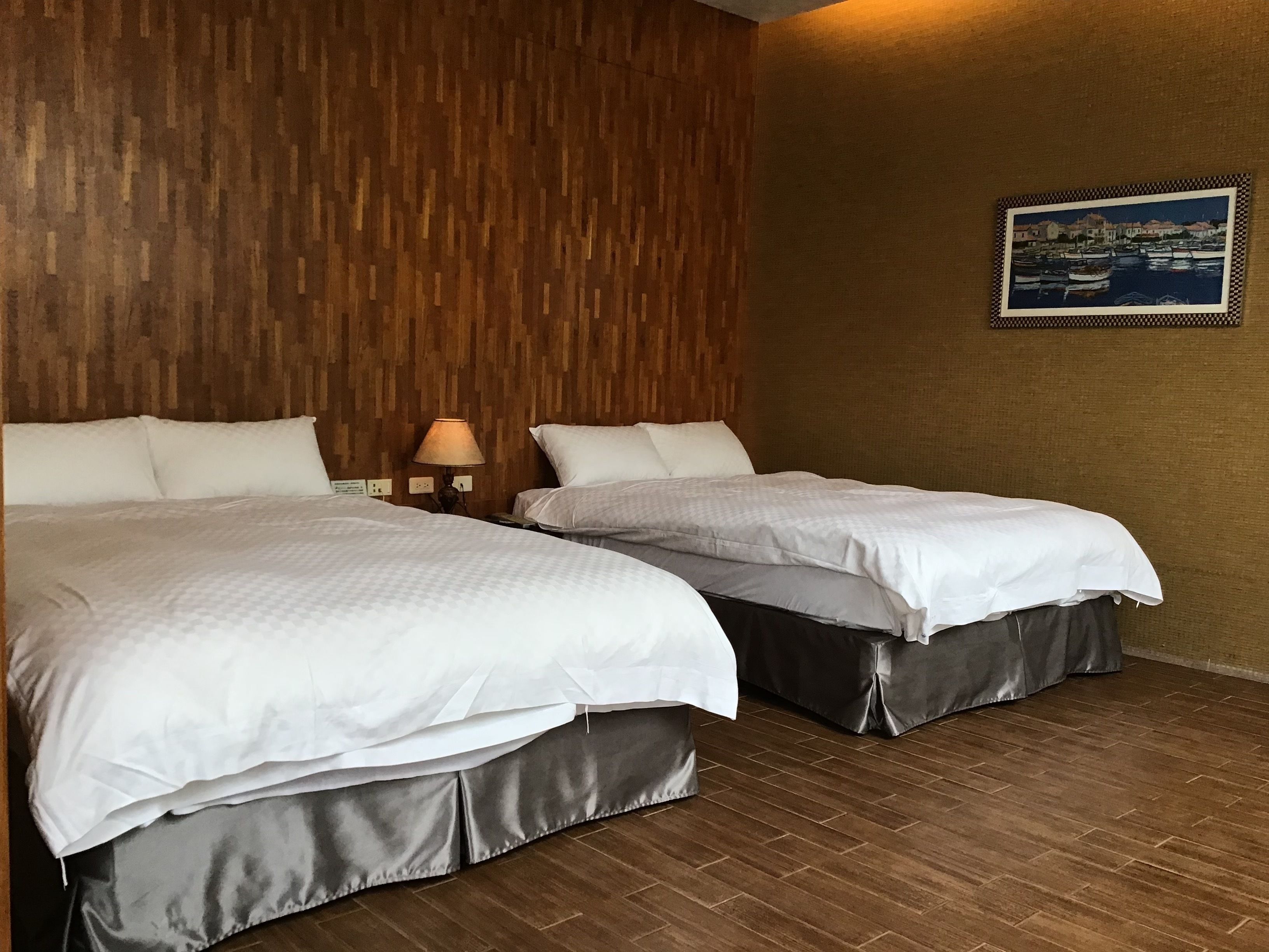 A hotel room with two beds, wooden paneling on the wall, a framed picture, and a lamp.