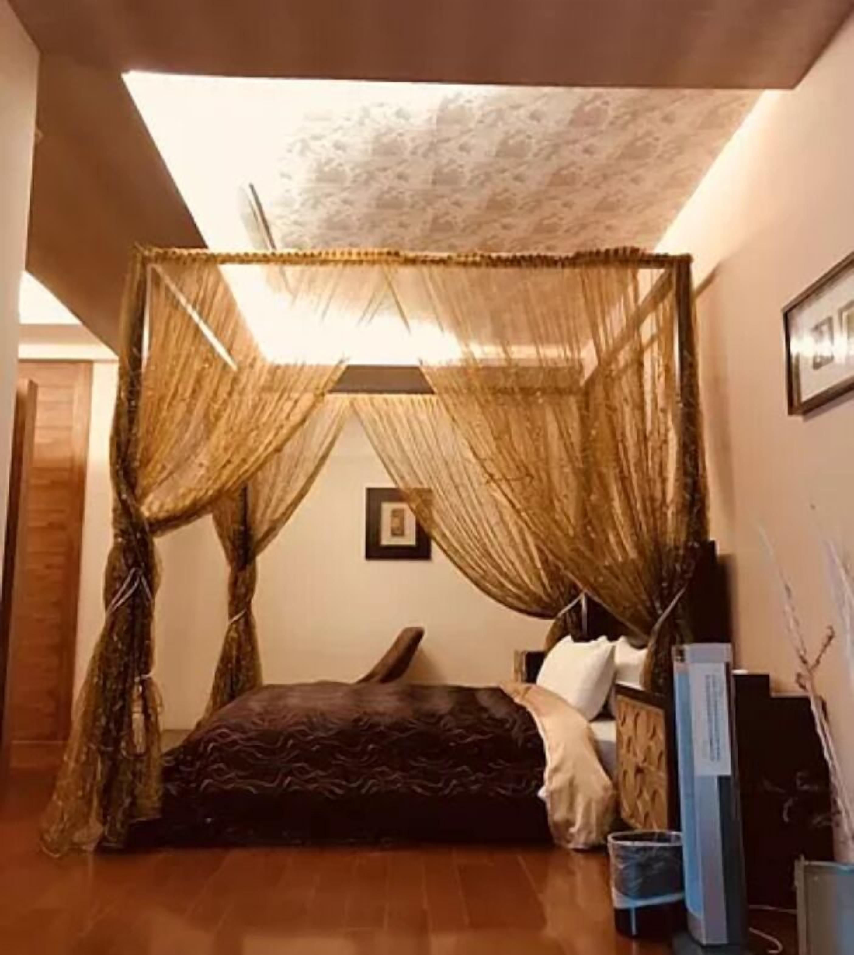 Un dormitorio con cama con dosel, una mesita de noche, un cubo de basura y un cuadro en la pared.