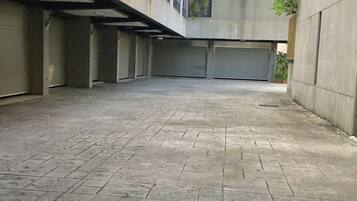 Un patio espacioso con suelo de baldosas, paredes de concreto y un edificio con varias ventanas y una puerta de garaje cerrada.