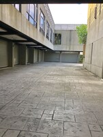 Un patio espacioso con suelo de baldosas, paredes de concreto y un edificio con varias ventanas y una puerta de garaje cerrada.