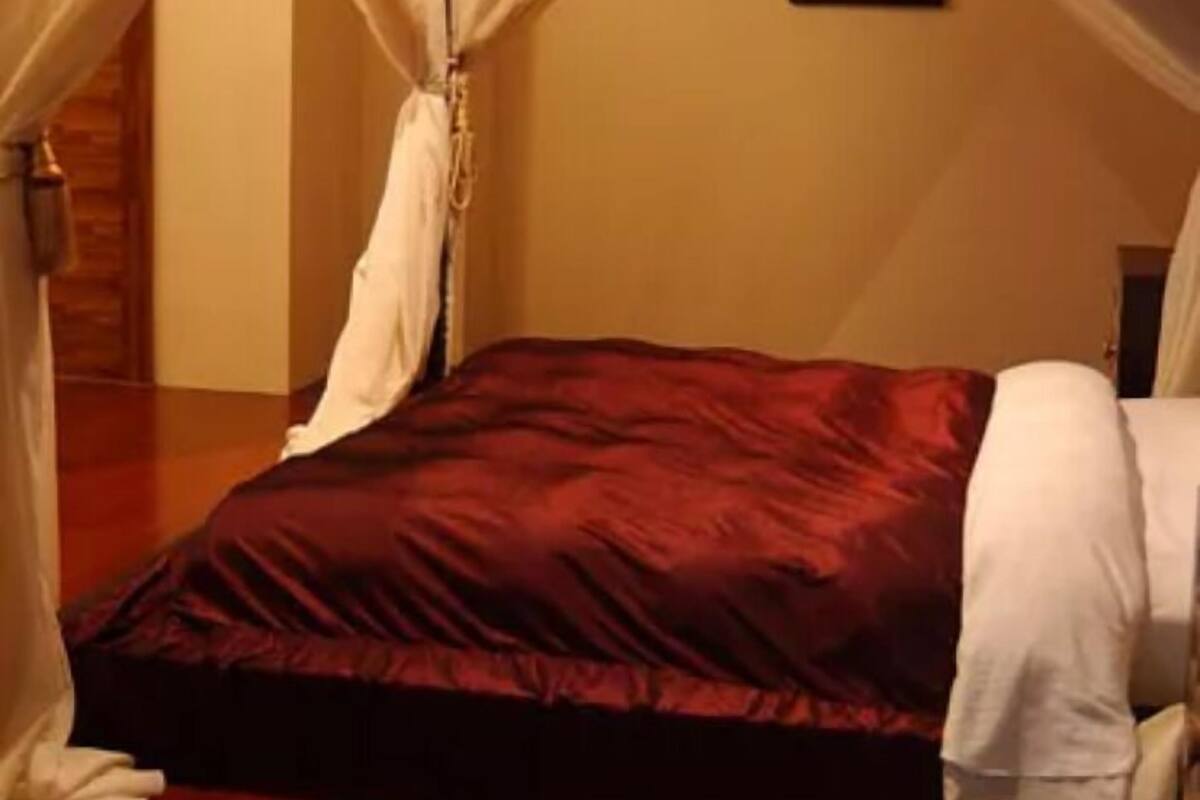 A bedroom with a bed, white curtains, and a framed picture on the wall.
