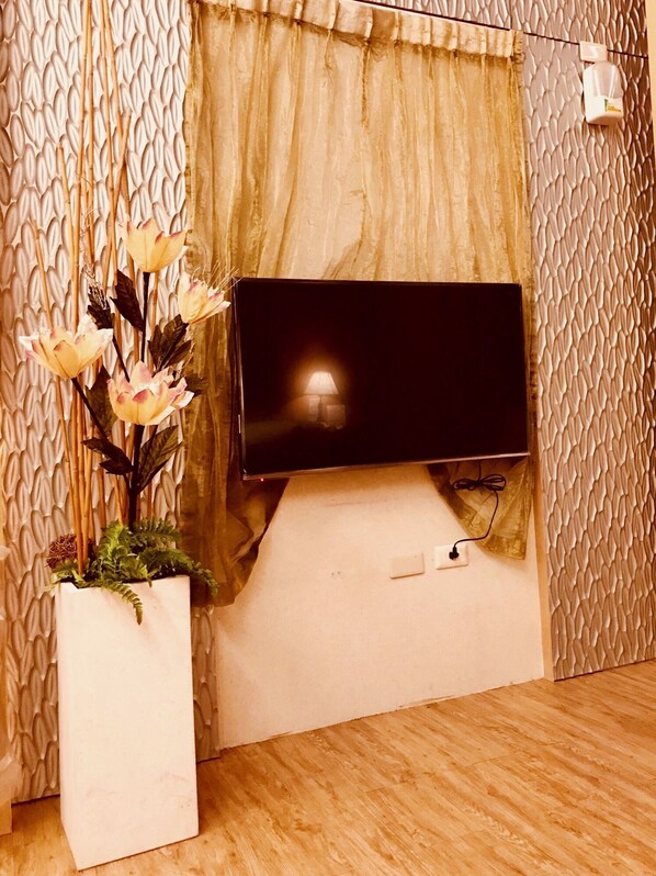 A flat-screen TV mounted on a wall with a textured pattern, a potted plant with flowers, and a wooden floor.