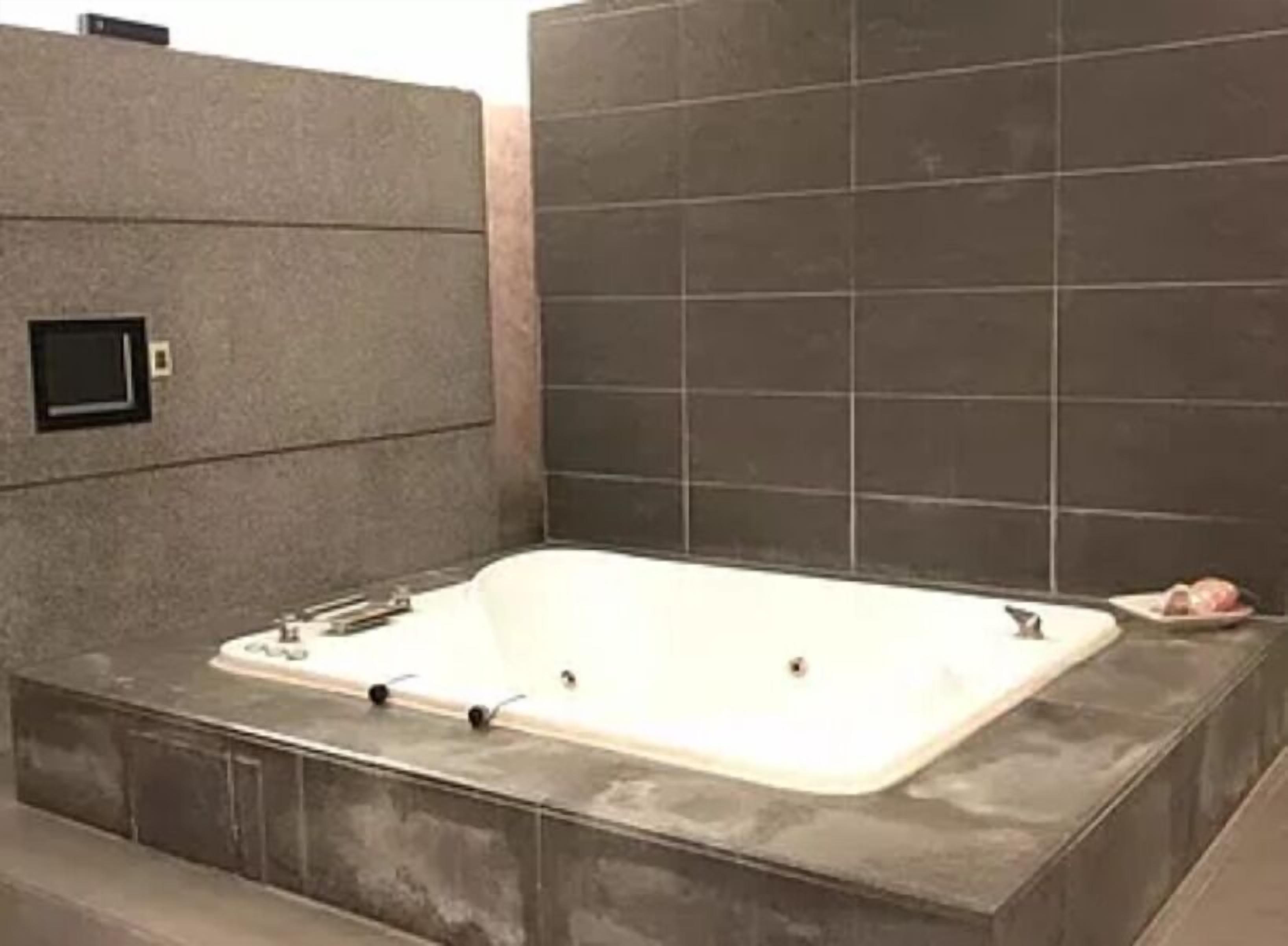 A modern bathroom with a large rectangular bathtub, a small window, and tiled walls.