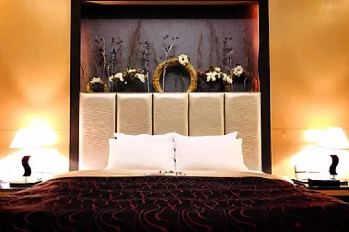 A hotel room with a bed, two bedside lamps, a headboard with decorative items, and a wall with a textured pattern.