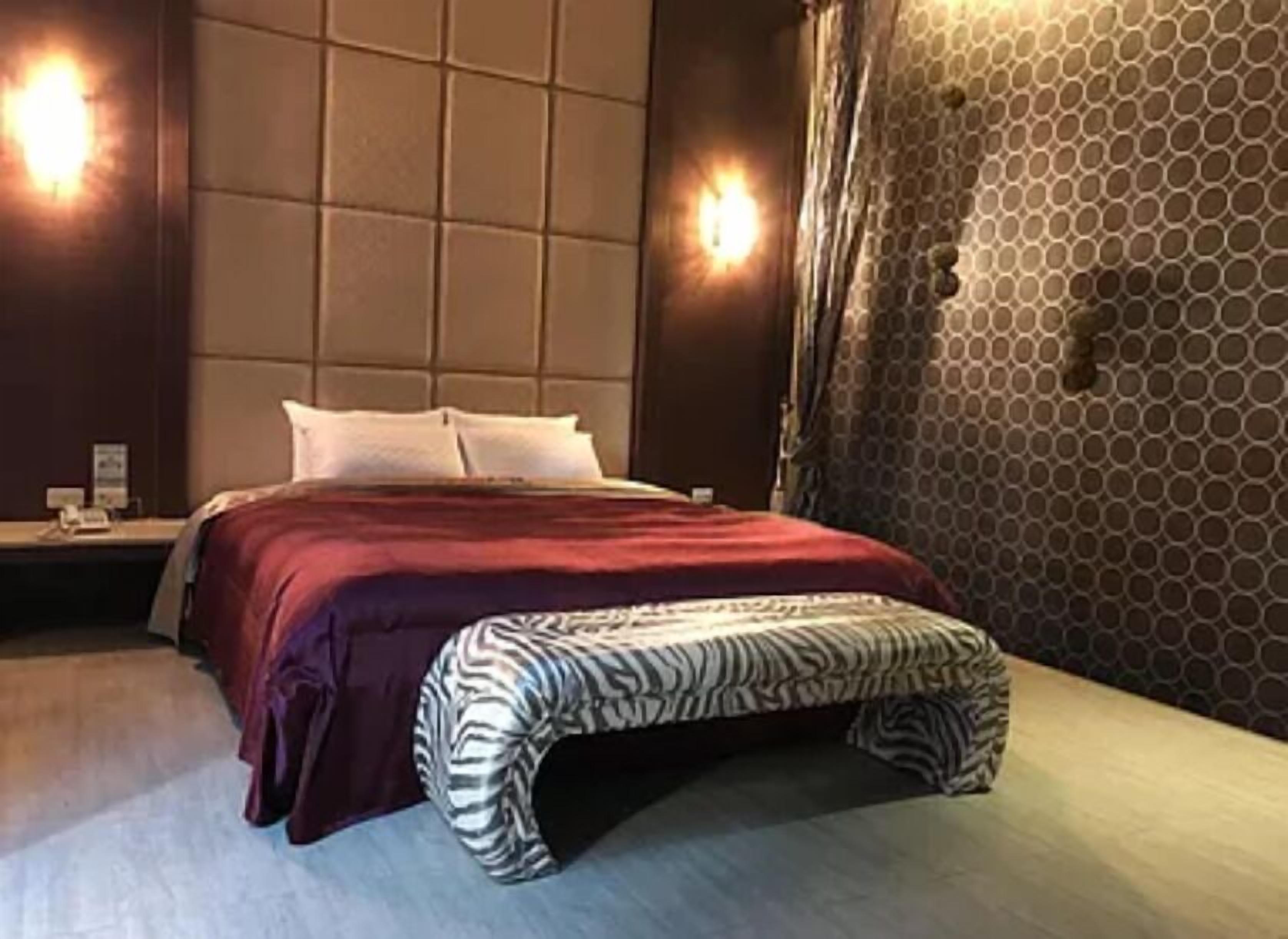 A hotel room with a large bed, a headboard with a geometric pattern, and two wall-mounted lights.