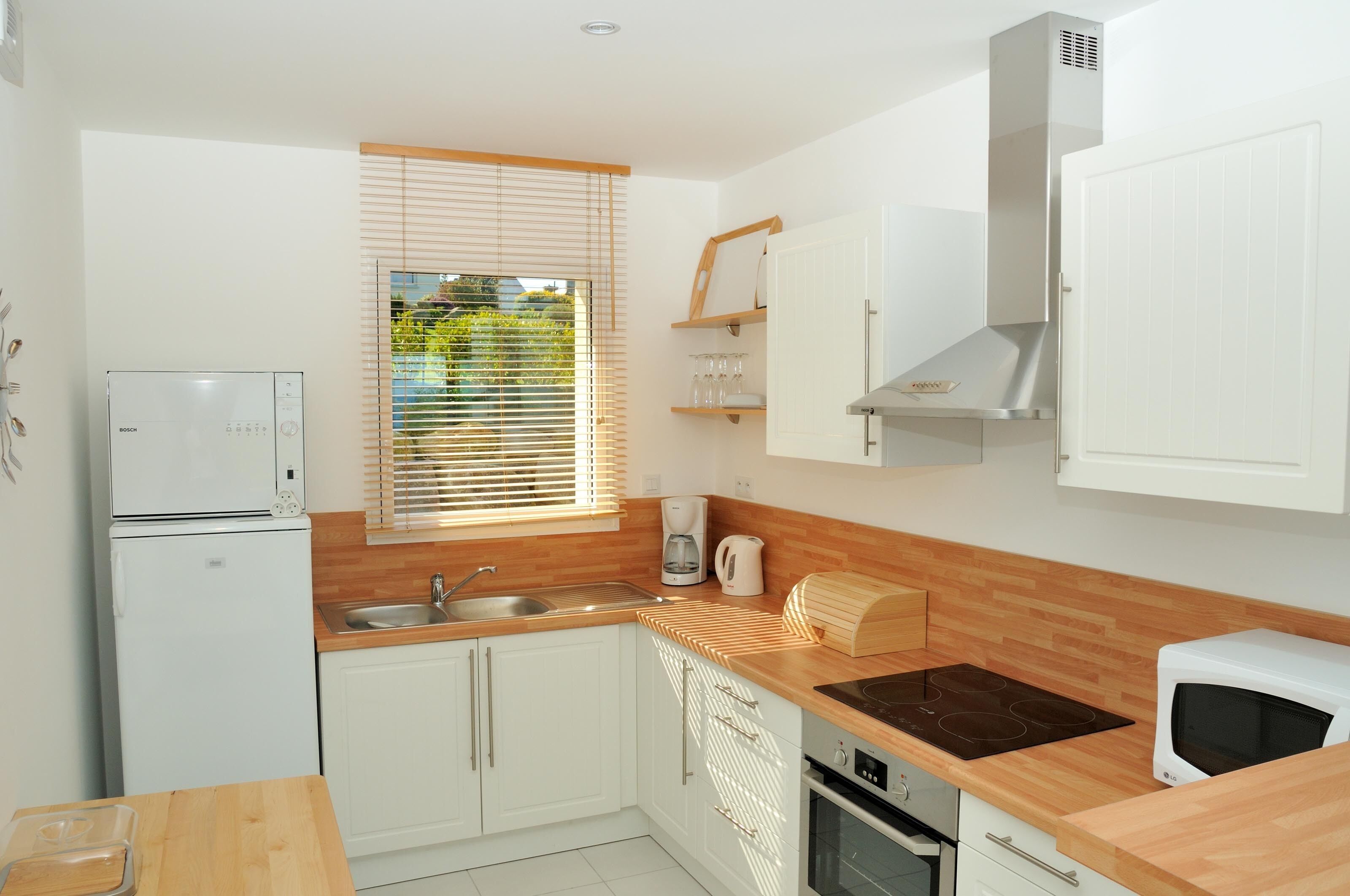 A compact kitchen with white cabinetry, a built-in oven, a microwave, and a coffee maker.