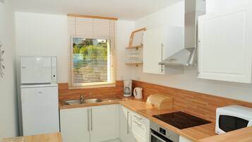 A compact kitchen with white cabinetry, a built-in oven, a microwave, and a coffee maker.