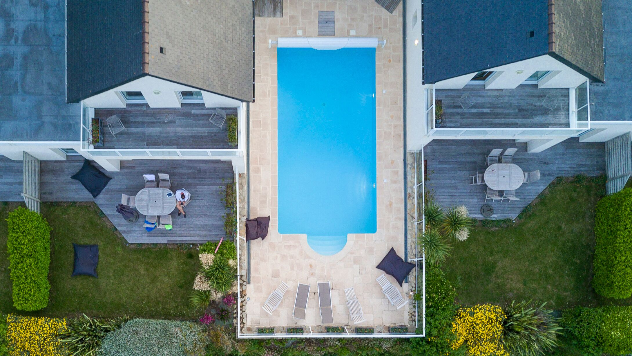 Ein modernes Haus mit einem zentralen Schwimmbad, zwei Terrassen mit Gartenmöbeln und einem gepflegten Garten.