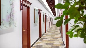 Un couloir d’hôtel avec des portes numérotées, un sol à motifs et un plafond avec des poutres en bois.