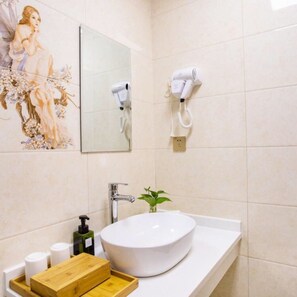 Un baño con un lavamanos blanco, un espejo, un secador de pelo y un cuadro decorativo en la pared.